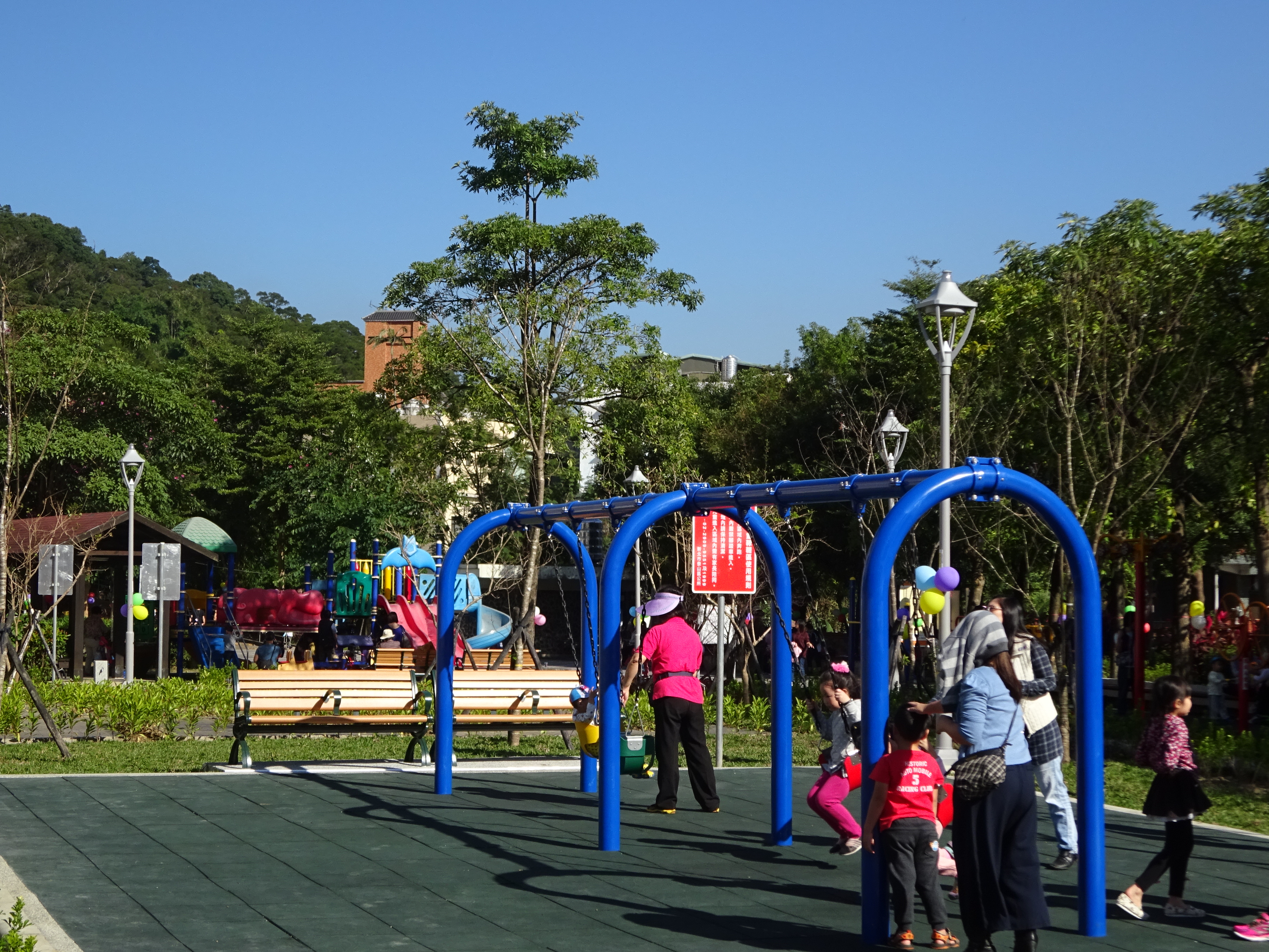 附近家長陪伴著孩子使用公園遊樂設施