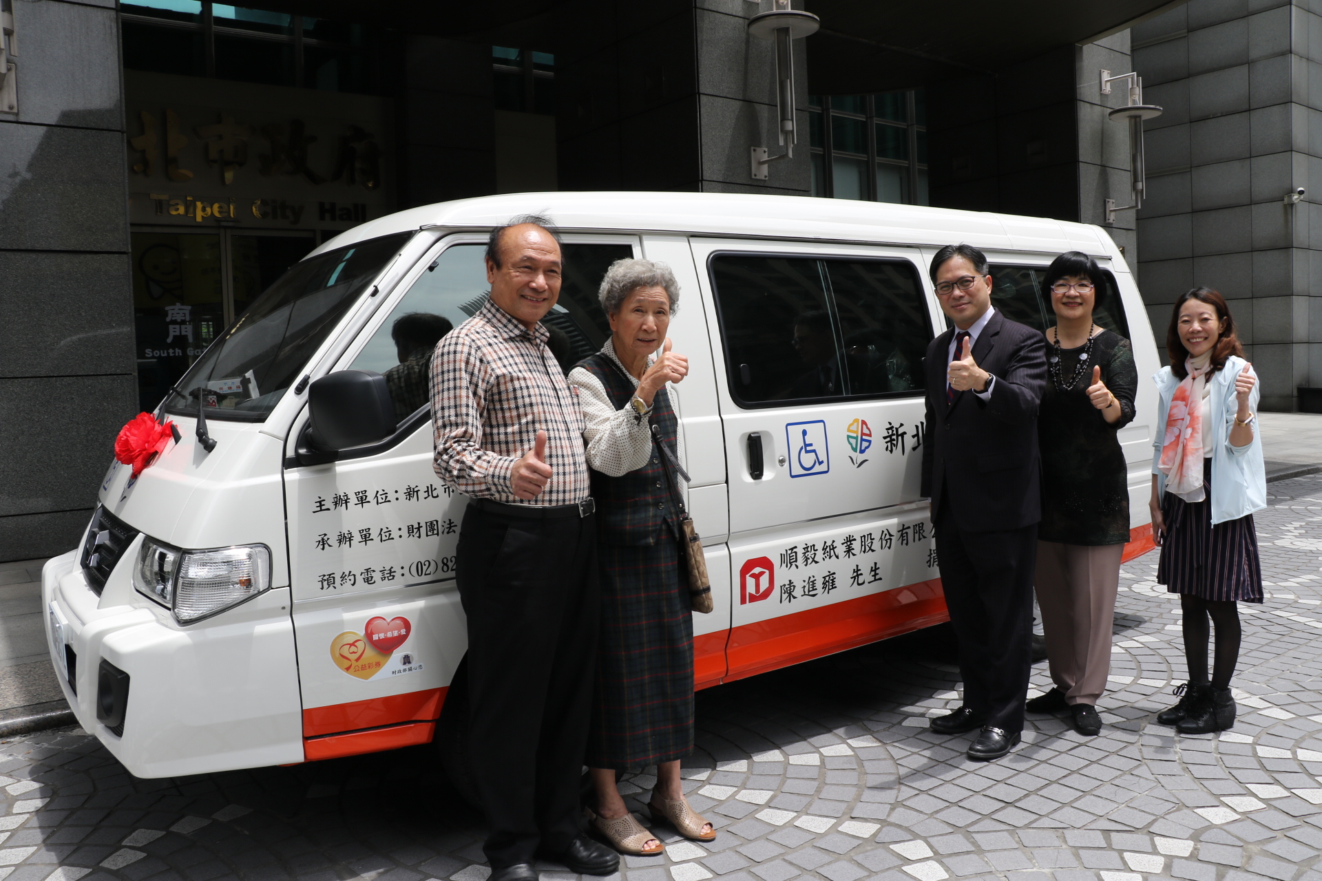 陳進步（左）和媽媽陳張抱捐贈新北市復康巴士   由副市長吳明機（右3）和社會局長張錦麗等人受贈