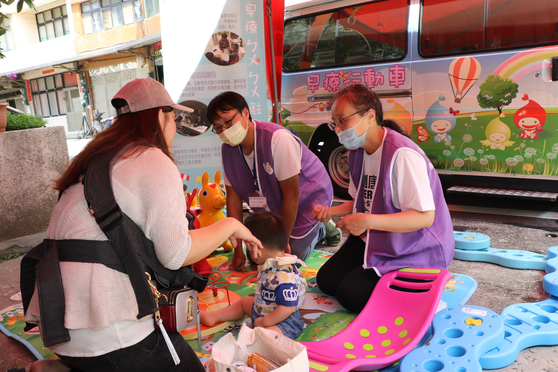新北市早療行動車開到石門偏區服務  早療教保員邱宜君（右）和社工督導蔡賀凱（中）幫家長篩檢並提供相關諮詢