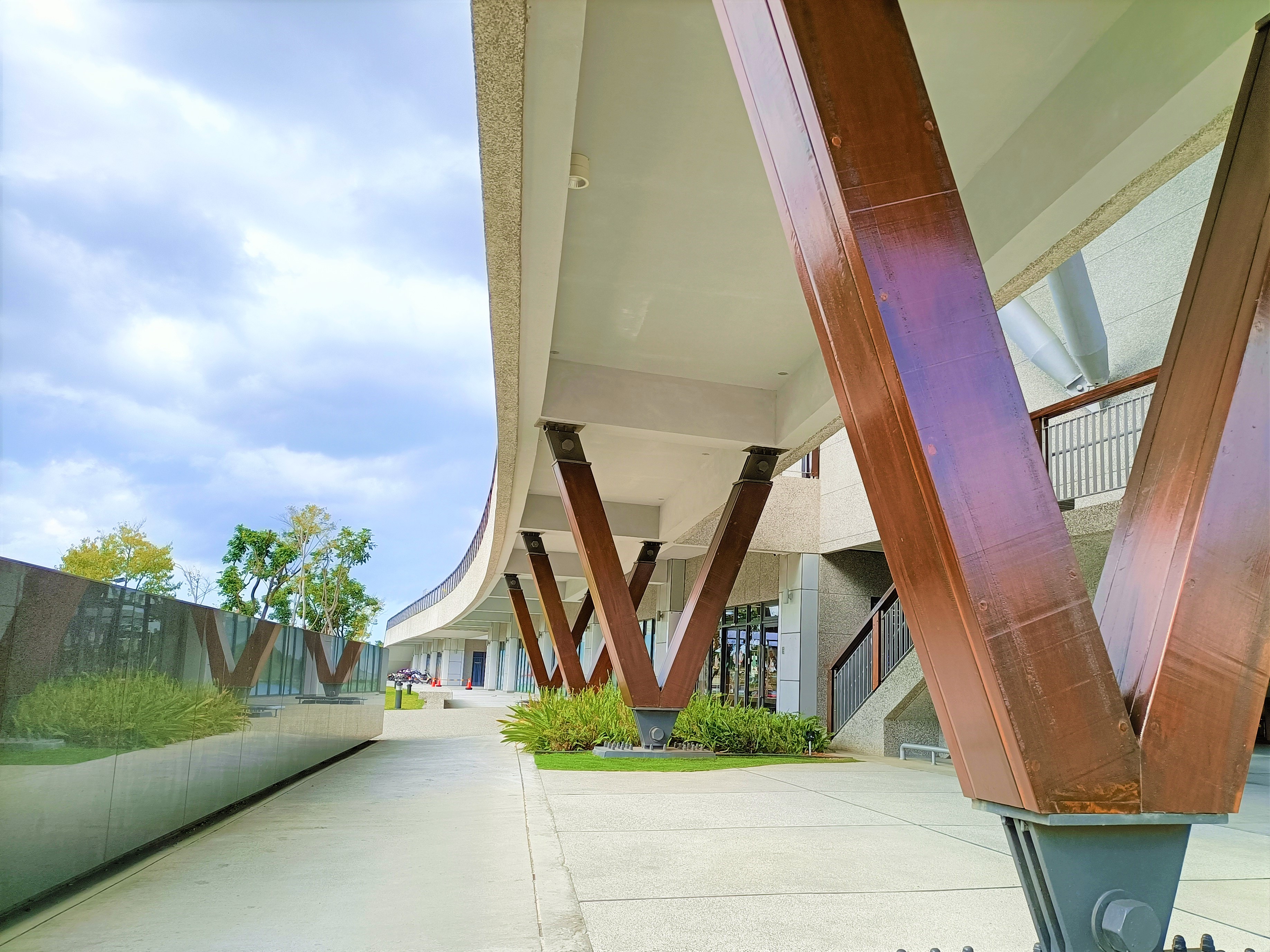 八里區公所西南側開放的弧形廊道，應用鋼構結合木材塑造濱海棧道意象特色