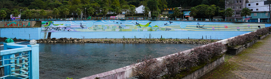 坪林區北勢溪茶博館前美化後的護岸彩繪，在北勢溪清澈的溪水映射及純白色調的茶博館襯托下，整幅壁畫彷彿如躍然紙上的畫。 