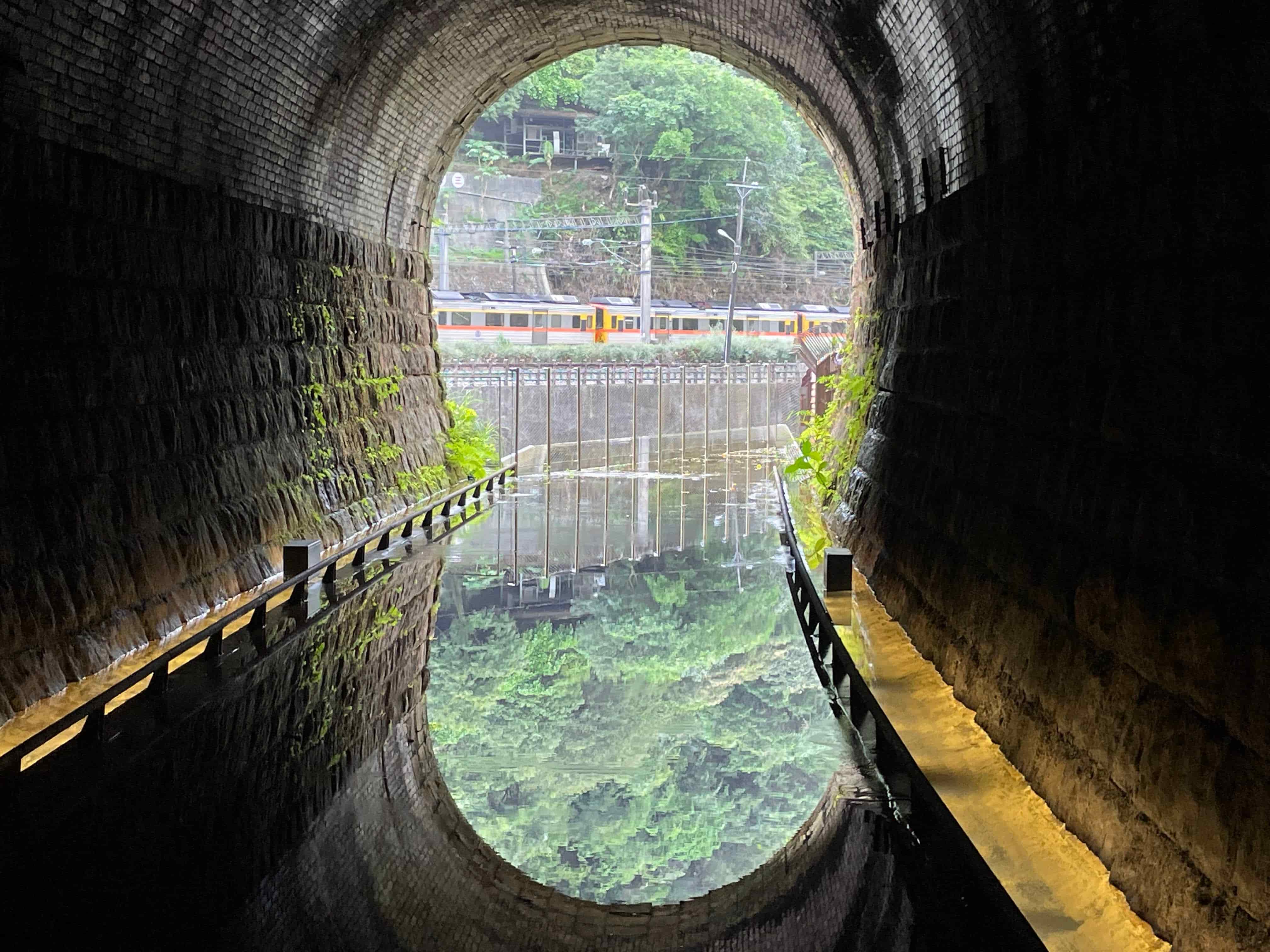在三瓜子隧道設計的鏡面水池反射出翠綠山色及火車行經影像。