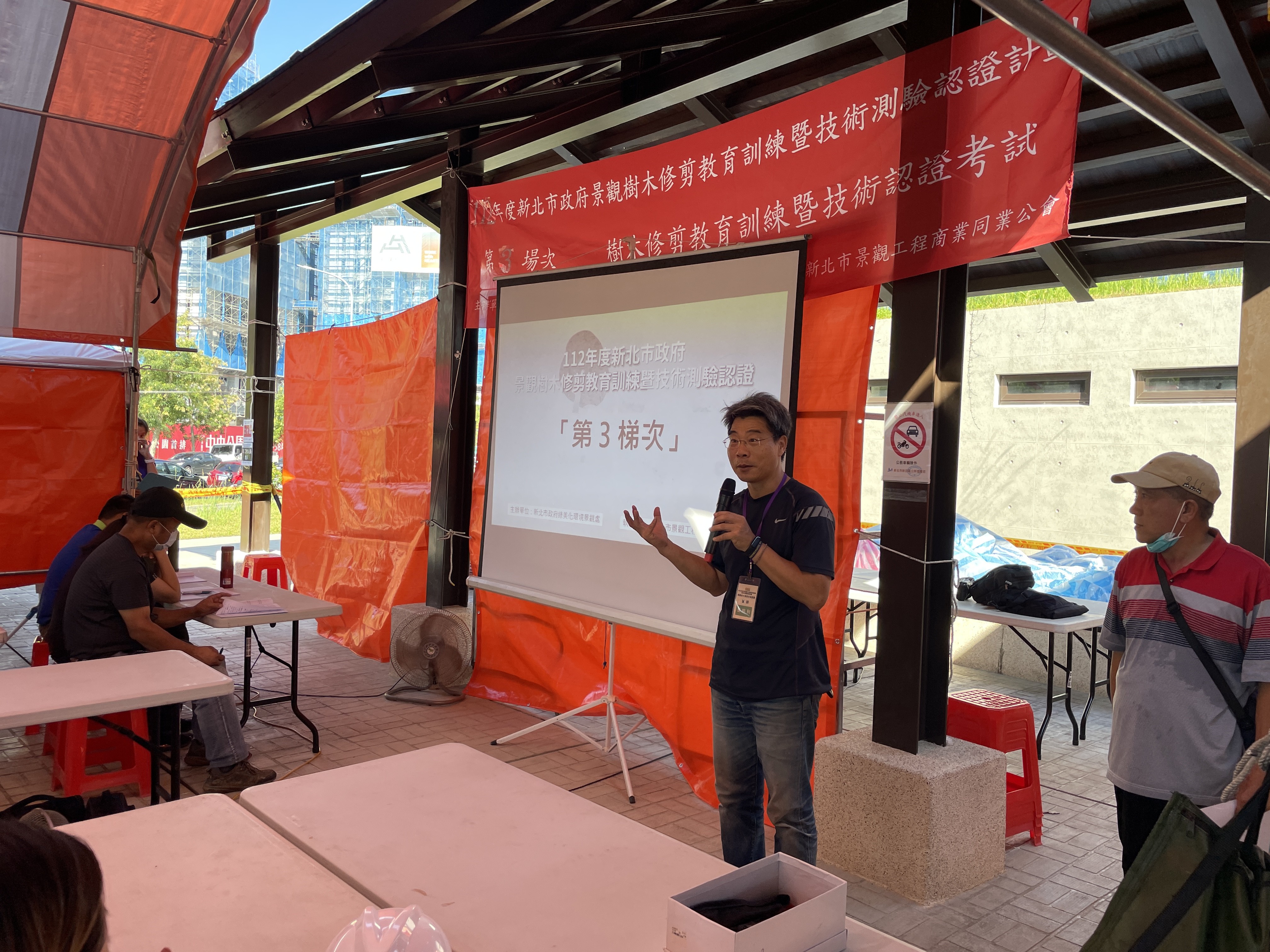 景觀處邀請臺灣省園藝技師公會副理事長曹明利老師帶領學員們到戶外實地演練，以實例講解如何正確安全地使用工具進行樹木修剪作業，圖為演練前之說明