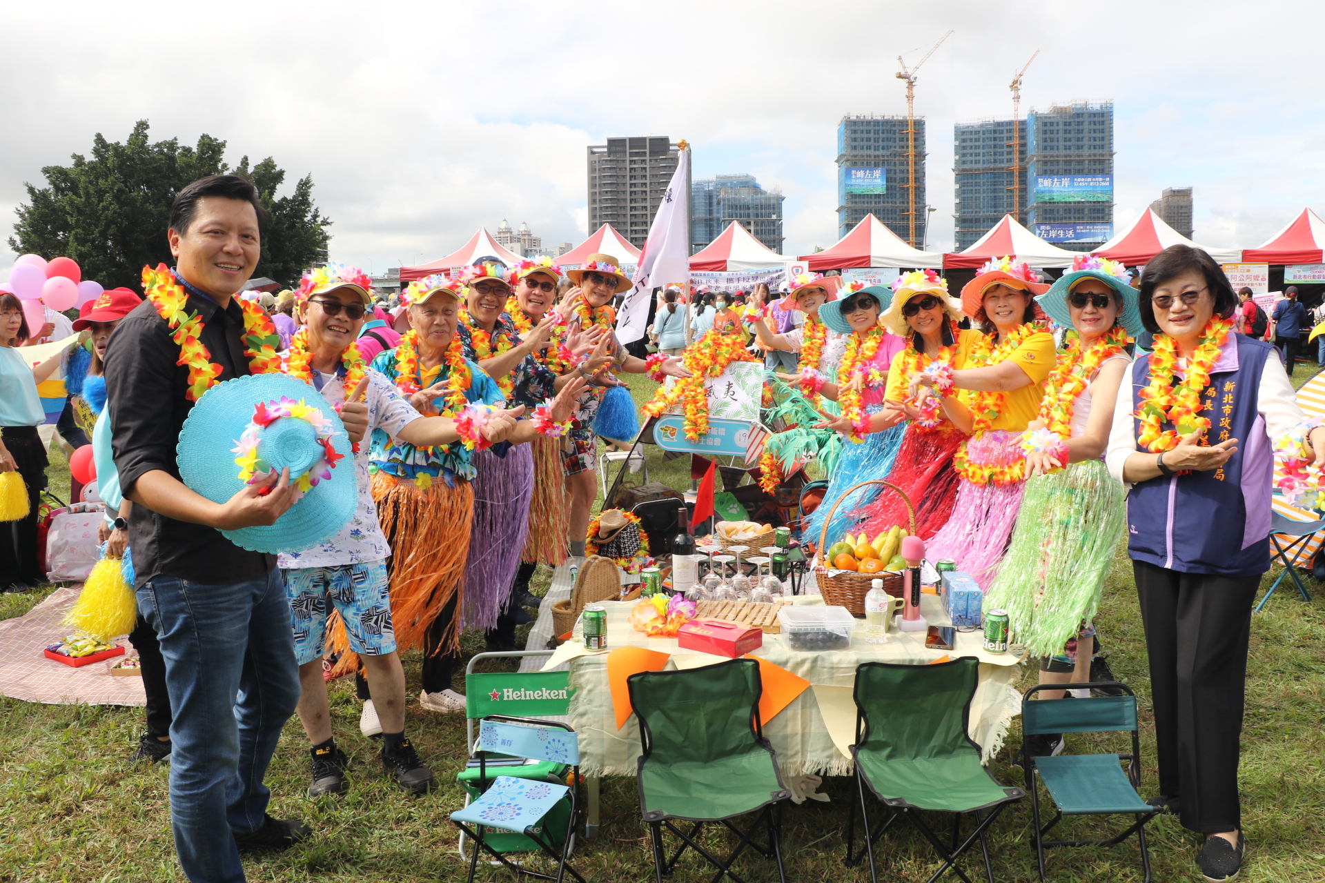  朱惕之一一繞場露營野餐趣攤位 被一群打扮成夏威夷女郎的志工包圍 右1為社會局長李美珍