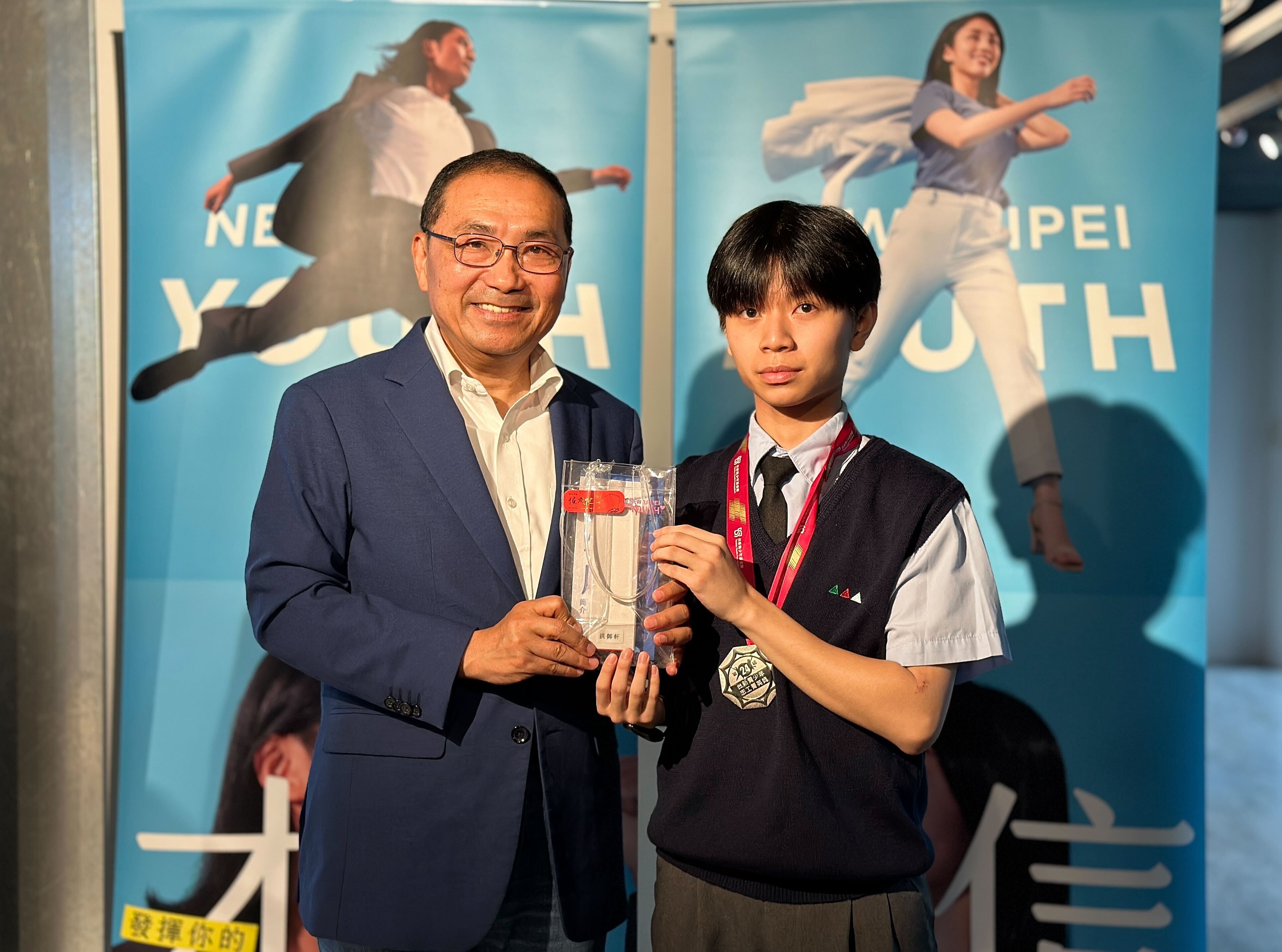 侯市長頒贈禮品予榮獲台新青少年台新青少年志工菁英獎傑出志工獎的洪御軒同學(圖右)。