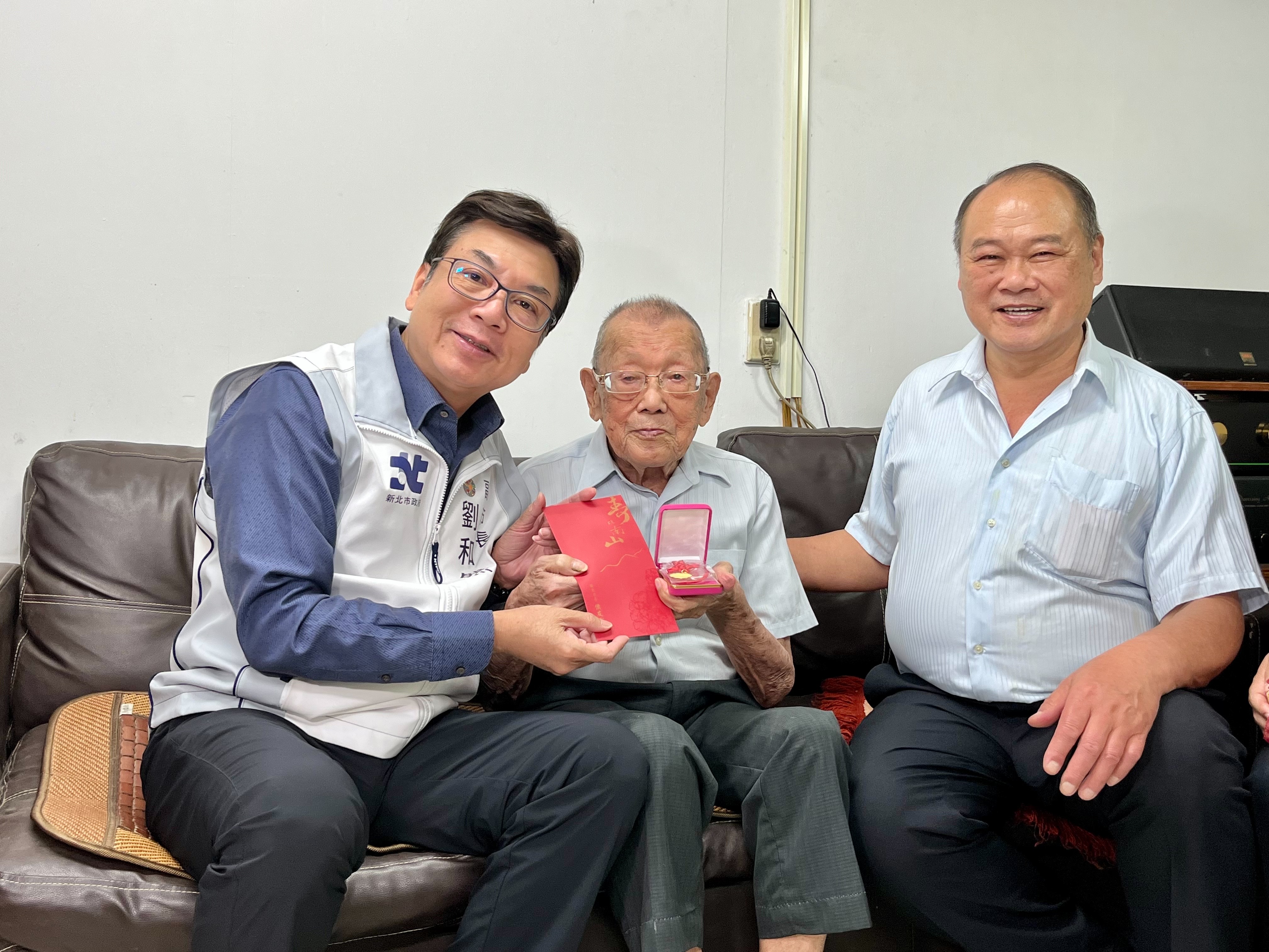 新北市副市長劉和然(左1)送上重陽禮金及祝福金鎖片，給102歲的人瑞林鏡鑾(中)，祝福健康平安。