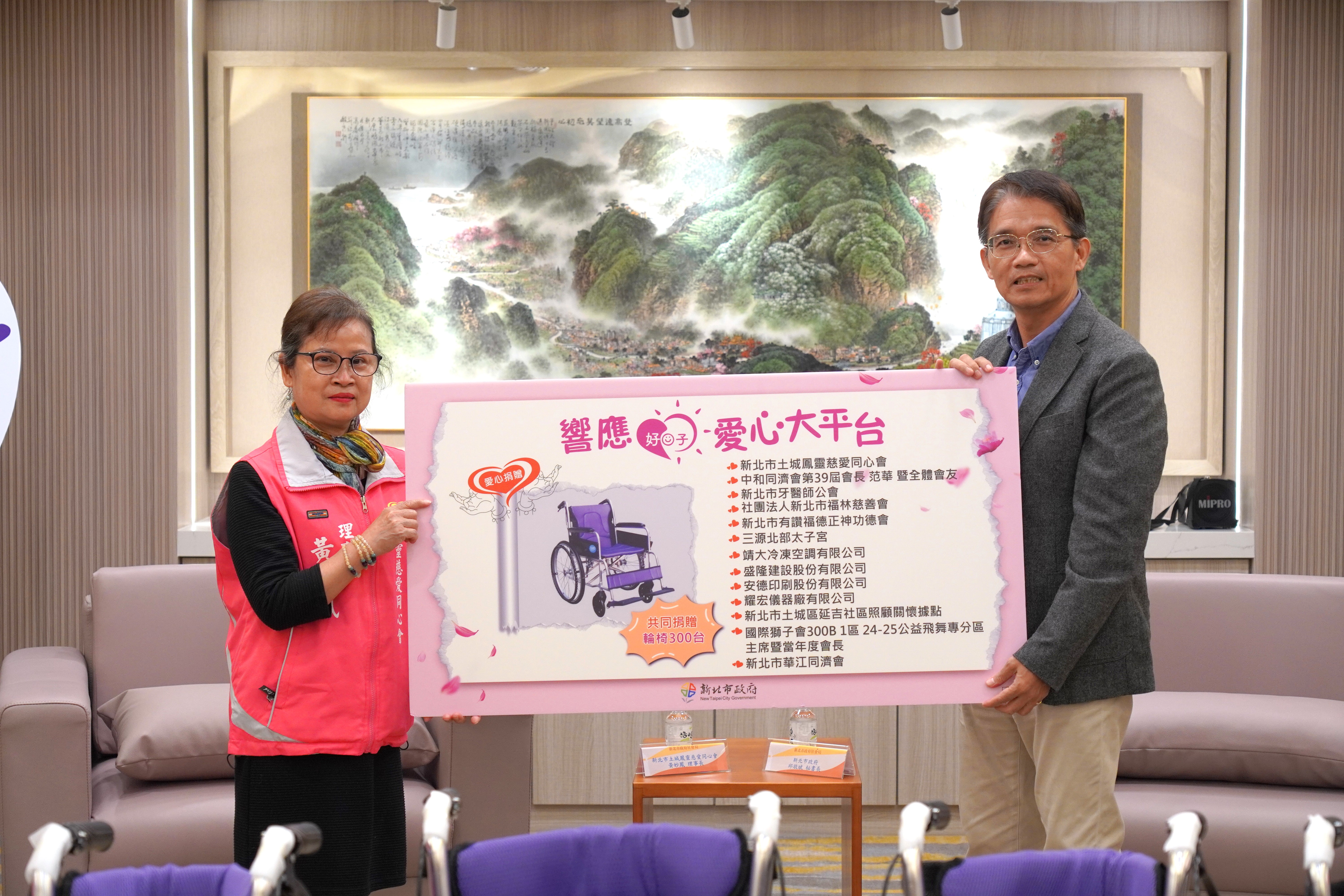 新北土城鳳靈慈愛同心會攜手民間13個單位捐贈300台輪椅給新北市，由土城鳳靈慈愛同心會理事長黃妙鳳(左)代表捐贈，新北市政府秘書長邱敬斌(右)代表受贈。