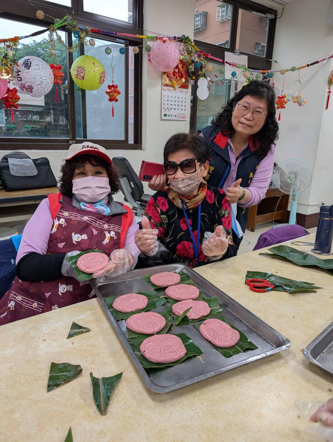 女力展現！社區媽媽與志工開心展示剛完成的紅色鼠麴粿，笑容滿溢。