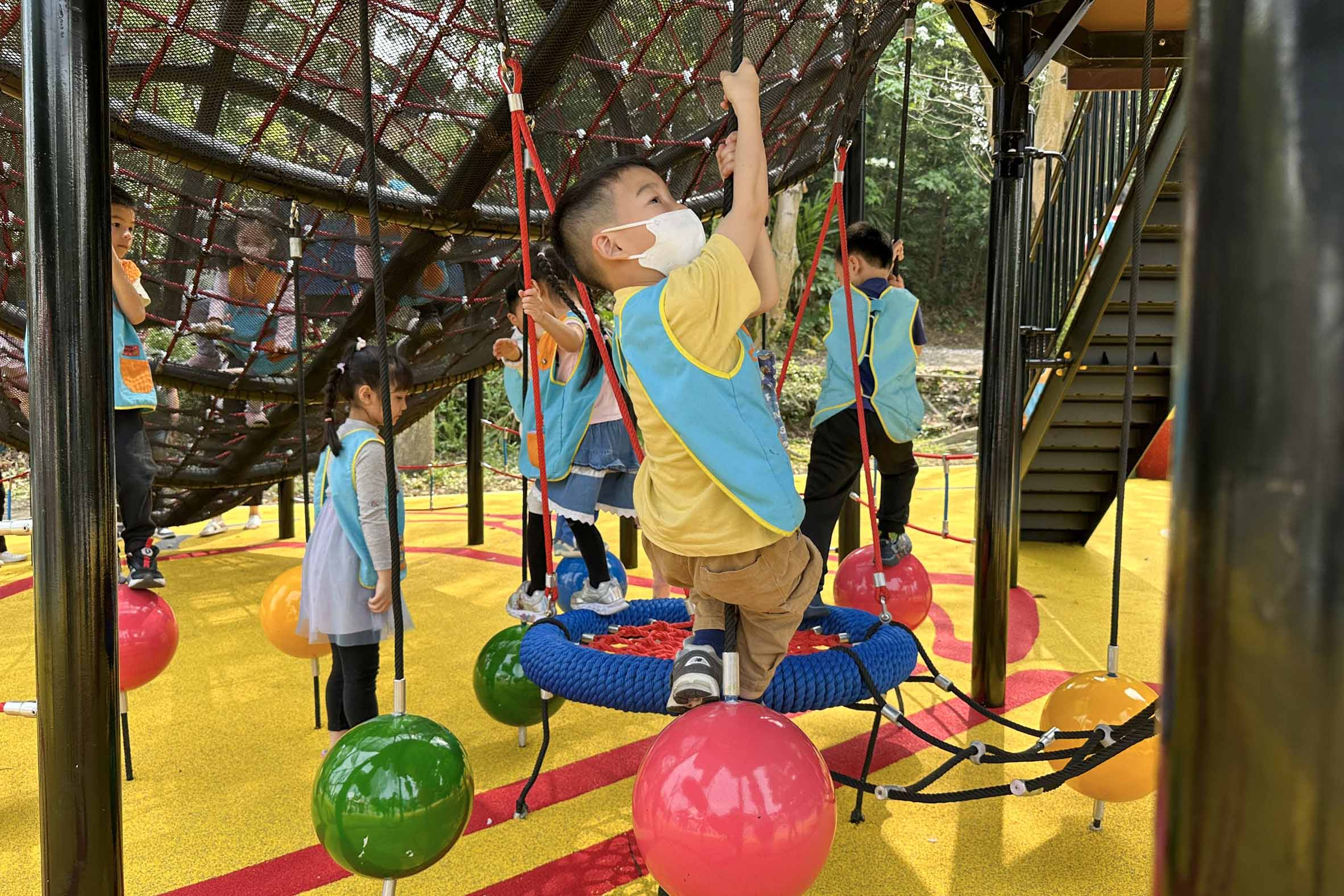 幼兒園孩童在鍬形蟲攀爬架下球型搖擺，提升肢體協調與反應能力
