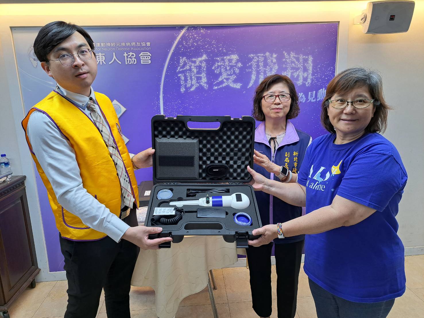 三重獅子會會長陳宏熺（左）代表捐贈拍痰機和眼控滑鼠給漸凍人協會 由理事長吳仕玫（右）代表受贈 中為許秀能副局長