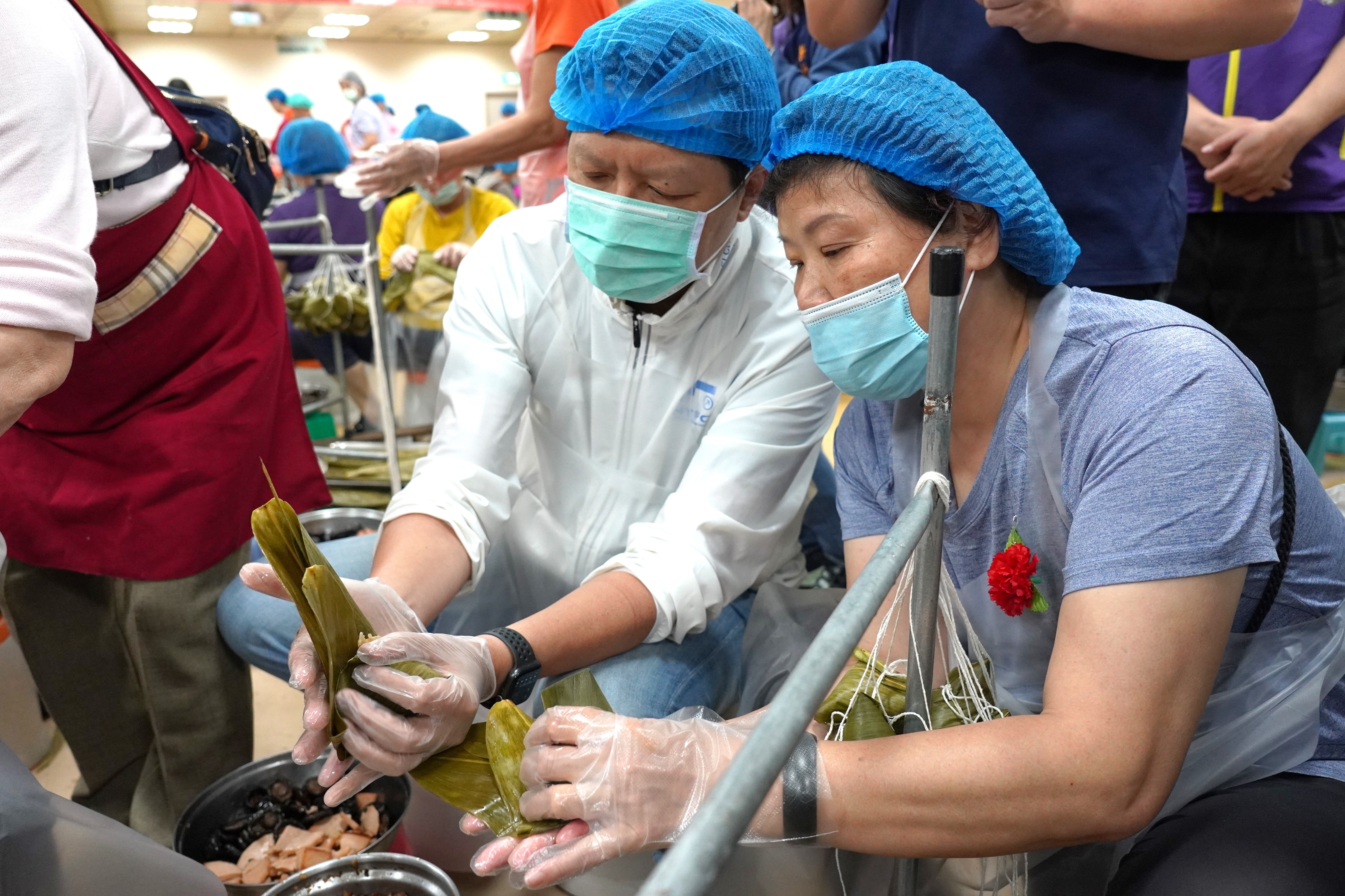 新北市副市長朱惕之(左)在志工指導下完成包粽