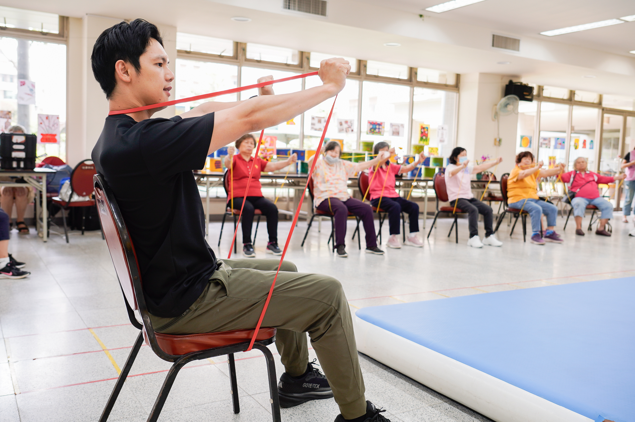 專業健身教練史提夫在健華新城社區照顧關懷據點帶領長輩使用彈力帶運動