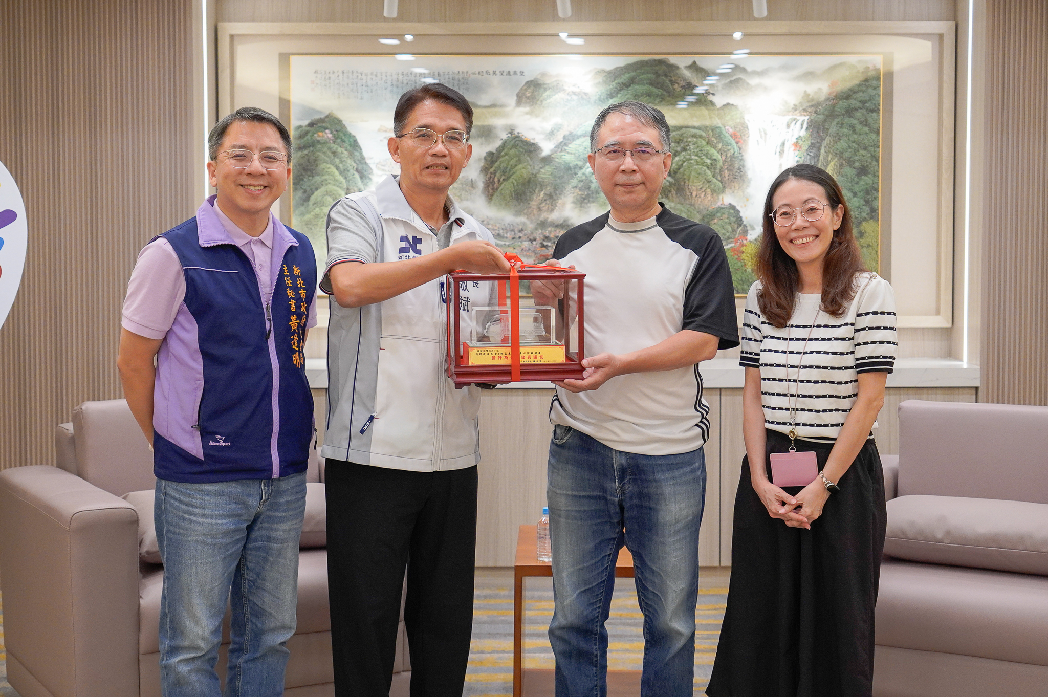  新北市政府秘書長邱敬斌代表侯友宜市長回贈復康巴士模型車給歐陽秋月的兄長歐陽培林（右2）紀念 左1為社會局主秘黃逢明 右1為交通局副局長林麗珠