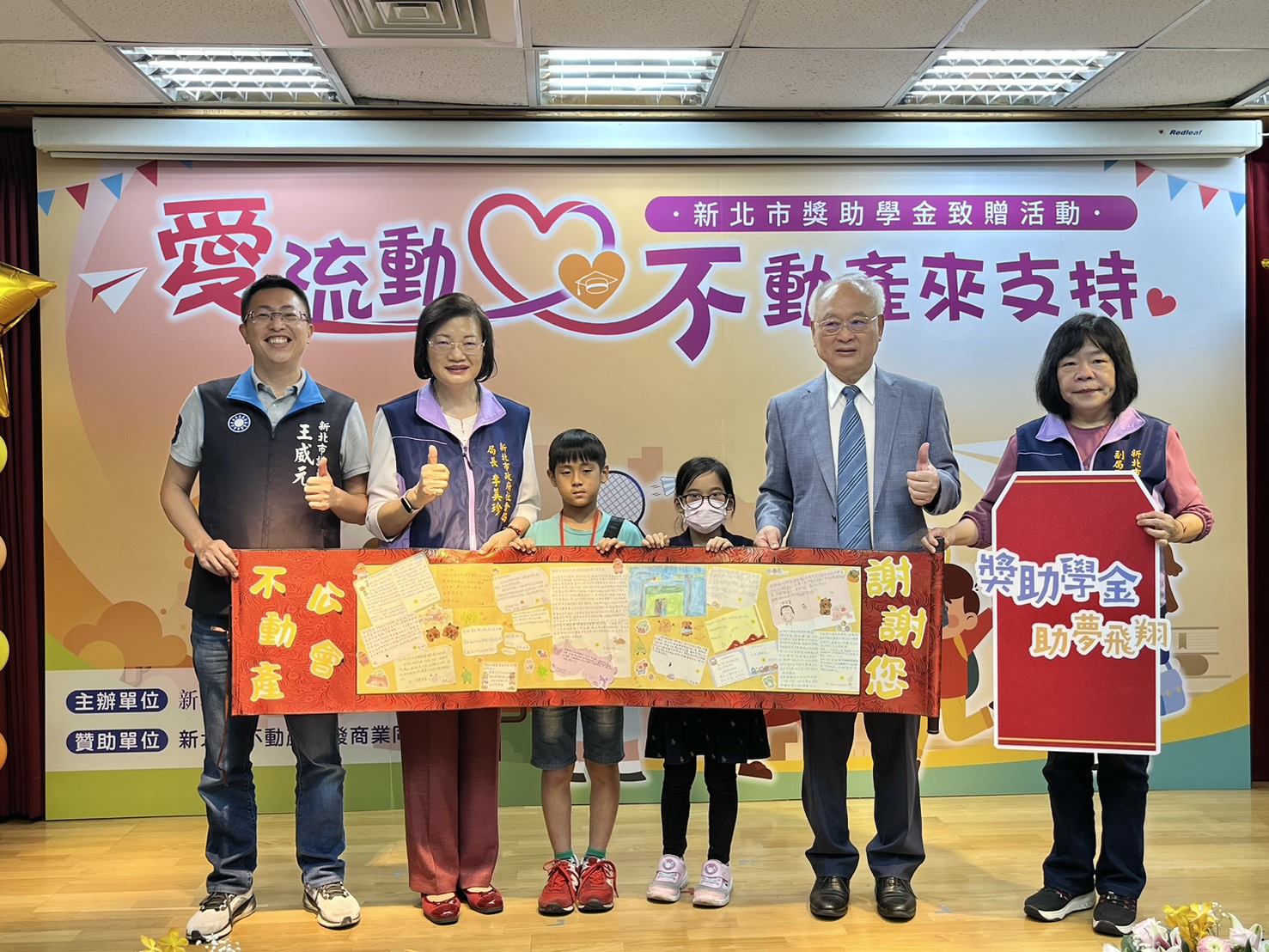 獲得獎學金的學生們手寫感謝卡，獻給新北市不動產開發商業同業公會廖志鴻理事長(右2)，並與新北市議員王威元(左1)、社會局長李美珍(左2)及副局長吳淑芳(右1)合影