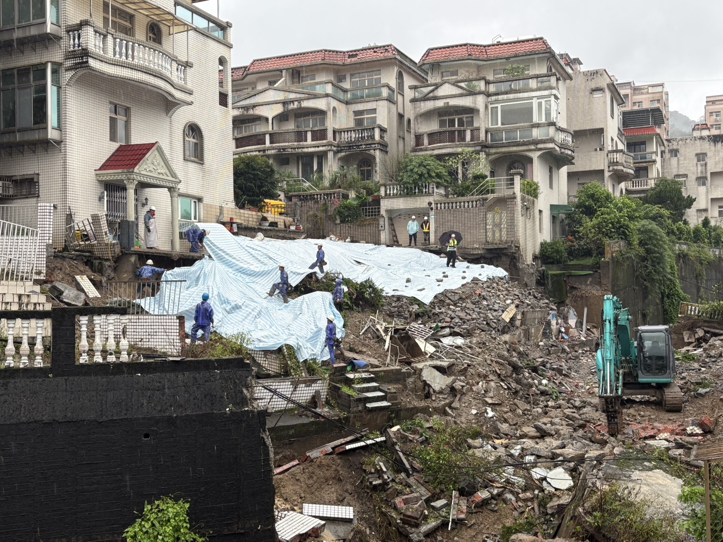 工務局持續進行搶災工程，邊坡覆蓋土方與帆布，減少雨水滲入擋土牆。