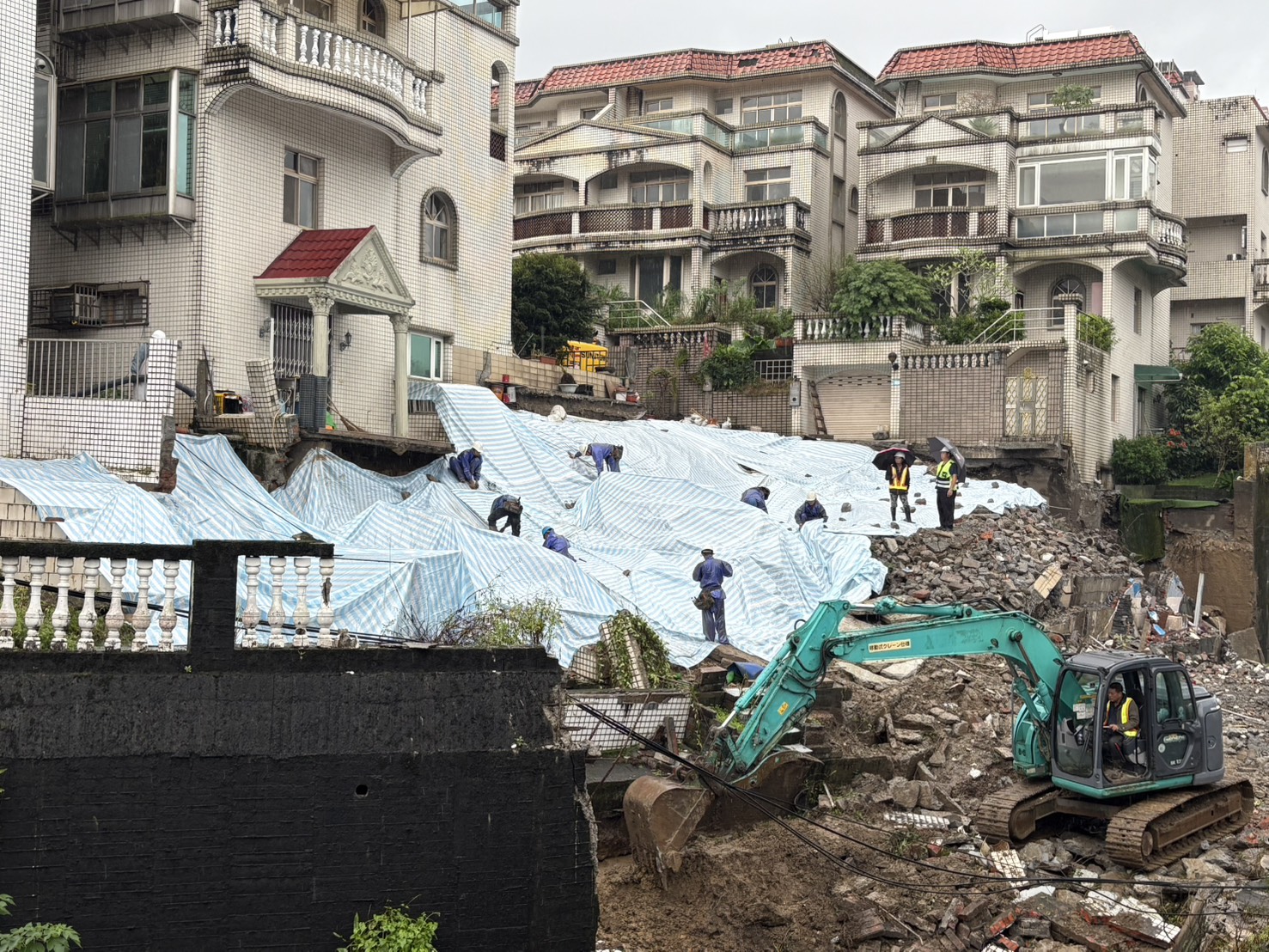 工務局調派人力與機具今日持續進行降土壓清坡作業，搶災人員到場覆蓋帆布加速搶災。