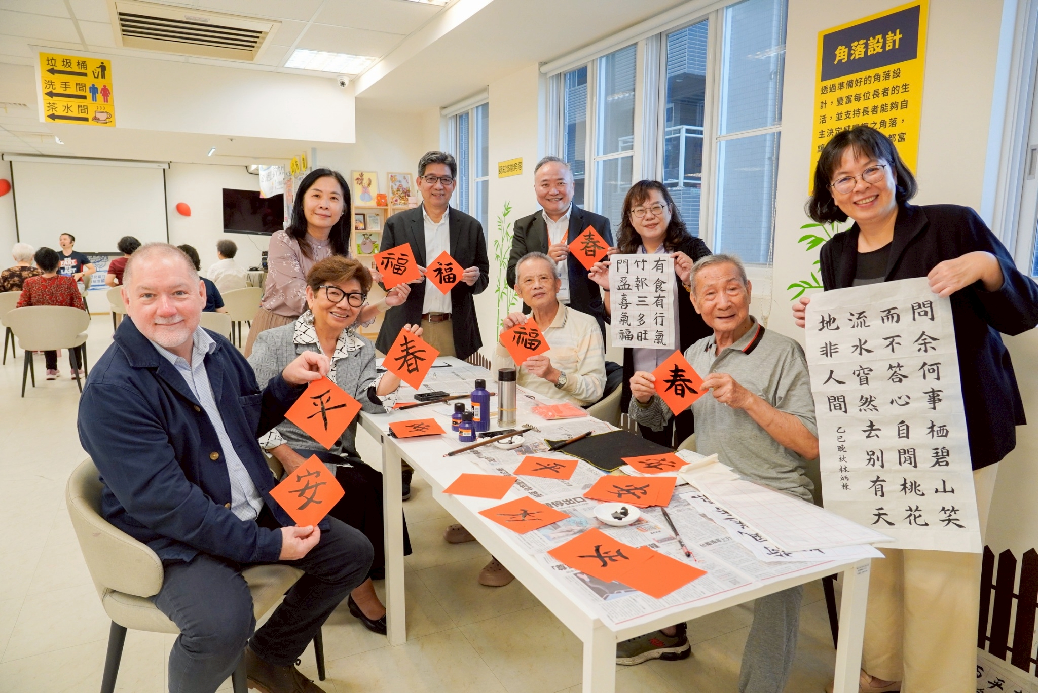 體驗書法活動後，Rick博士(左1)、譚孟春教授(左2)與社會局專門委員林秀穗(右3)等人手拿紅宣紙及書法作品合影留念