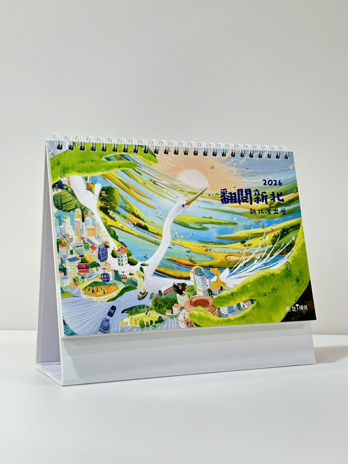 2026《新北潔出曆》封面設計以新北市鳥「鷺鷥」為主角，象徵潔淨與希望，牠振翅飛翔於天空，俯瞰著不斷更新的城市景致，感受新北的蛻變