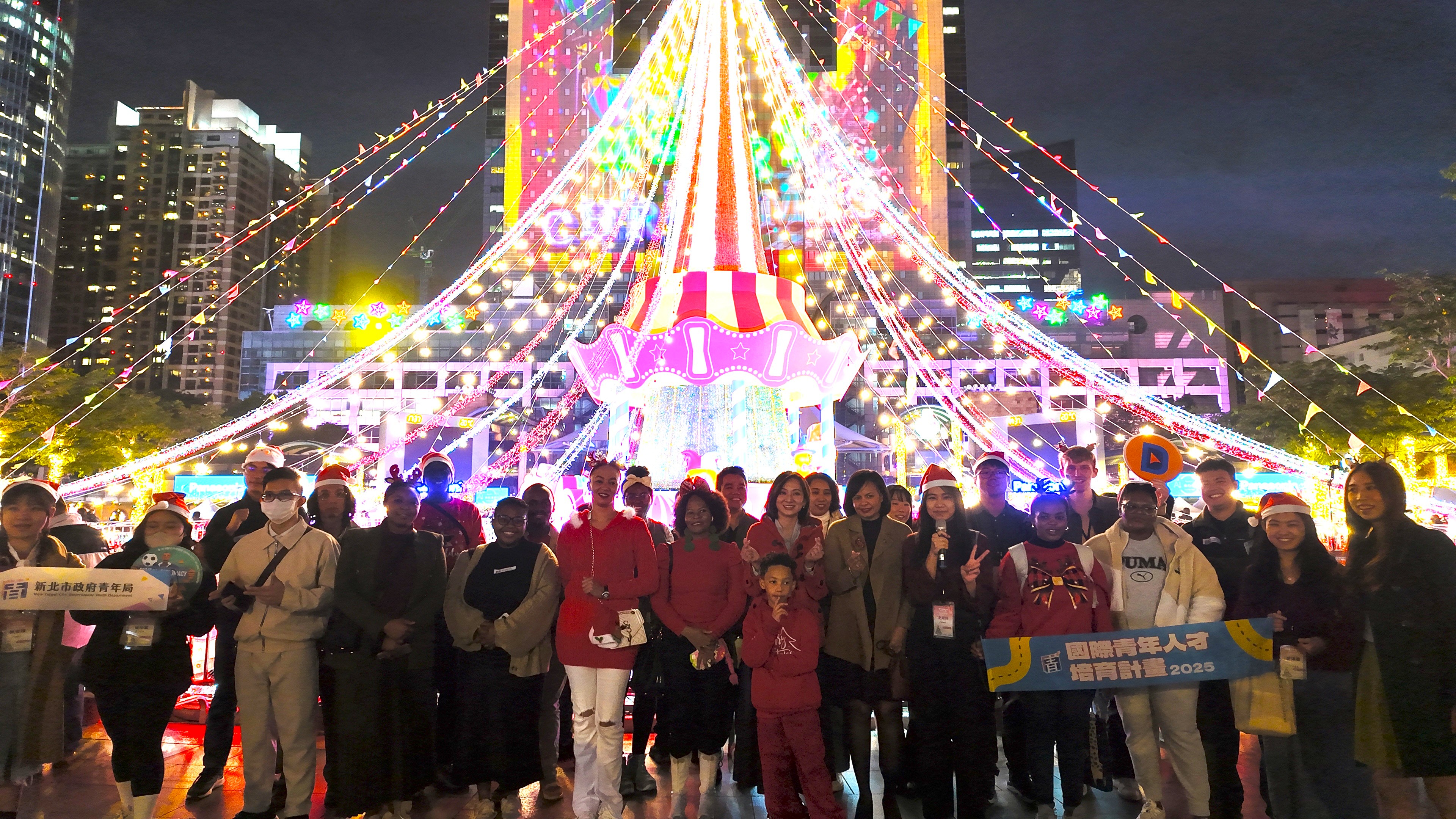 國際青年人才培育學員、大使及局長與外籍生於新北歡樂耶誕城聖誕燈前合照留念。
