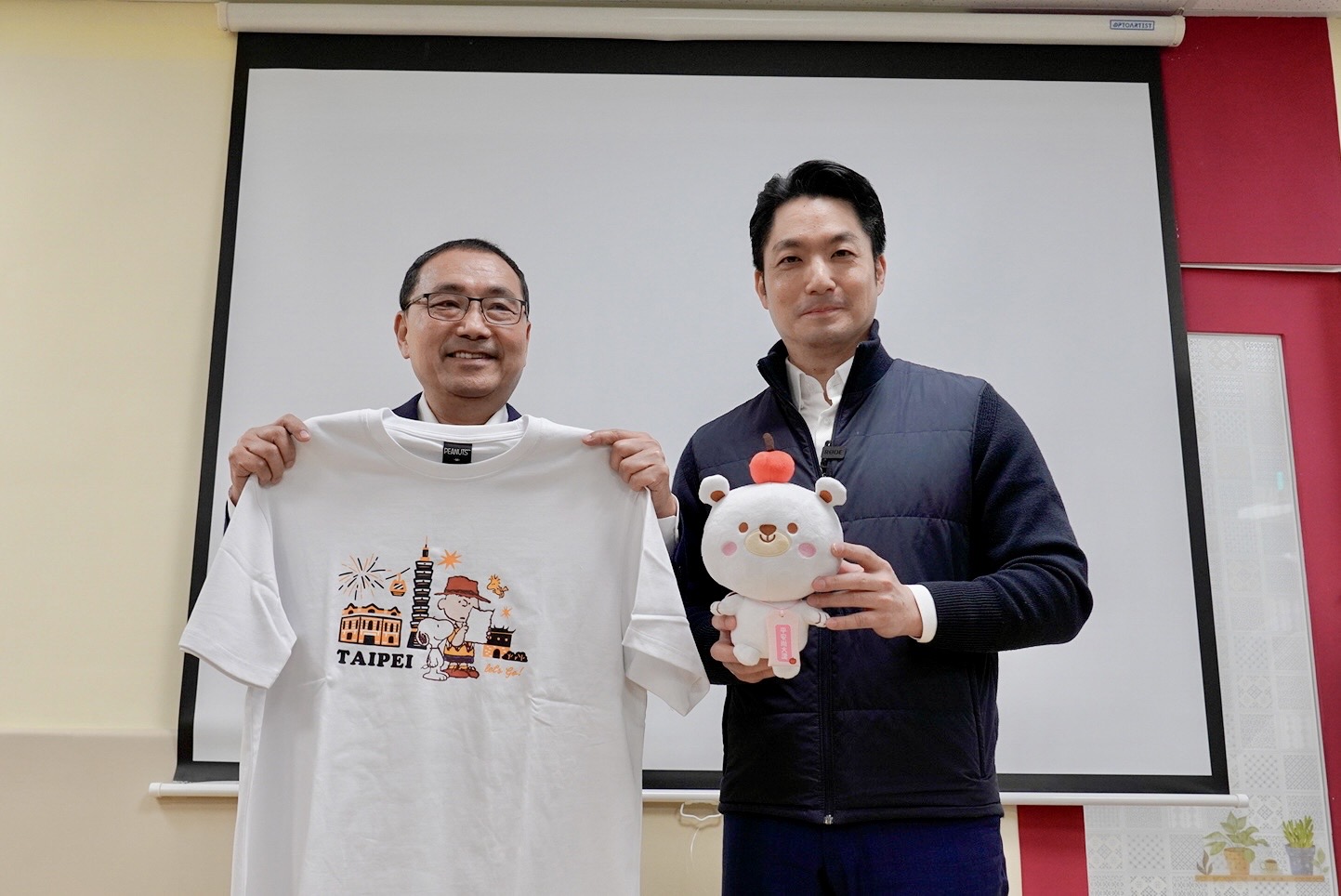 侯友宜致贈「新北愛小孩吉祥物 熊果」予蔣萬安，象徵雙北攜手守護孩子「平安長大」，蔣萬安則致贈史努比T恤、帽子等聯名周邊