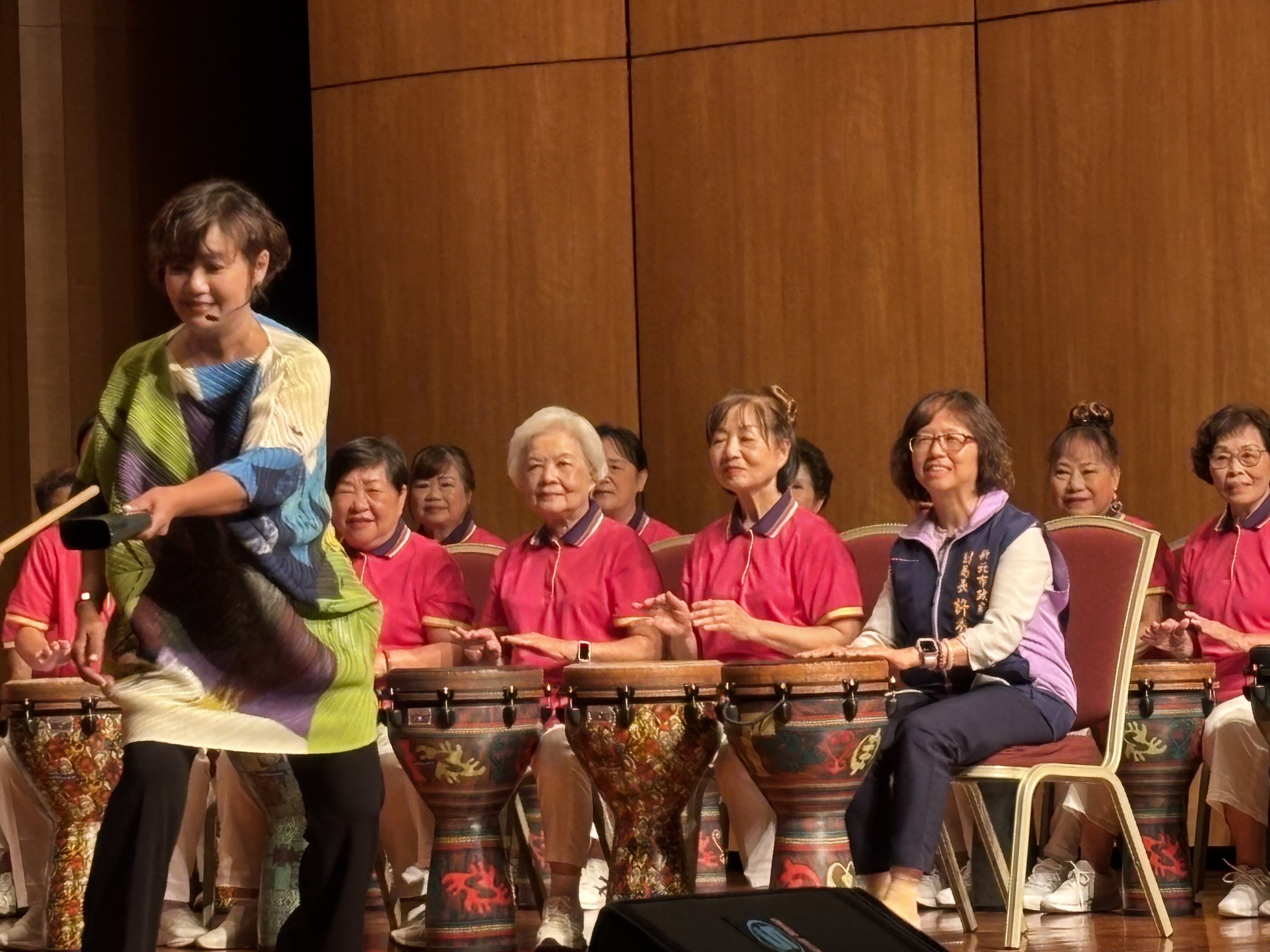 新北蘆洲功學社銀髮俱樂部舉行11週年成果展，社會局副局長許秀能(前排右一)與長者一同體驗打「墩杯鼓