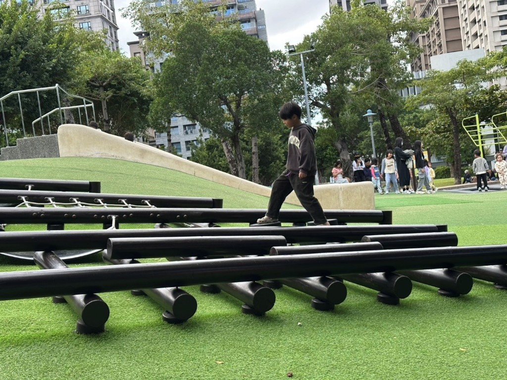 原木平衡遊具與地形高低變化相融合，提供孩童發展體能與平衡感的戶外空間。