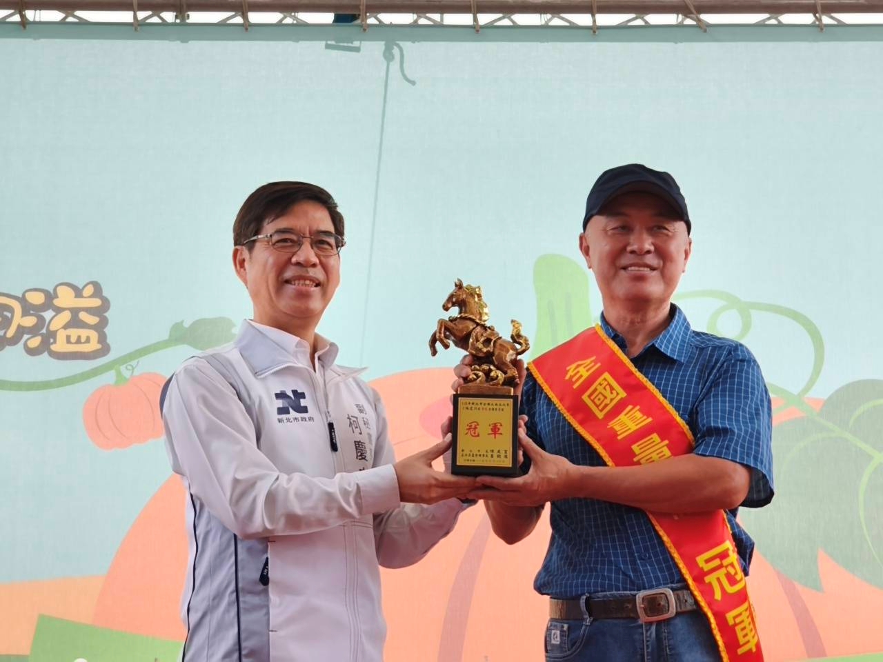 來自淡水區的農友林建訓(右)以重達773台斤的巨無霸南瓜勇奪重量組冠軍，也是第九度取得重量組冠軍頭銜，副秘書長柯慶忠(左)頒發獎座表揚