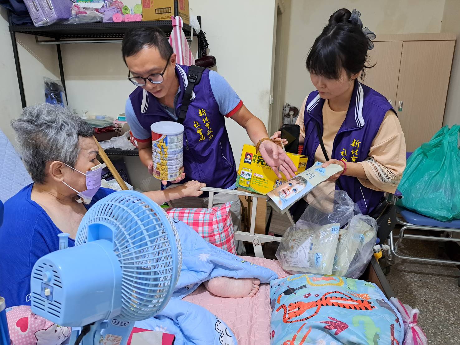 板橋第二社福中心主責社工徐志明（左）和主任陳玟伶帶著實物銀行生活物資奶粉、桂格完膳飲品等送給曹婦。