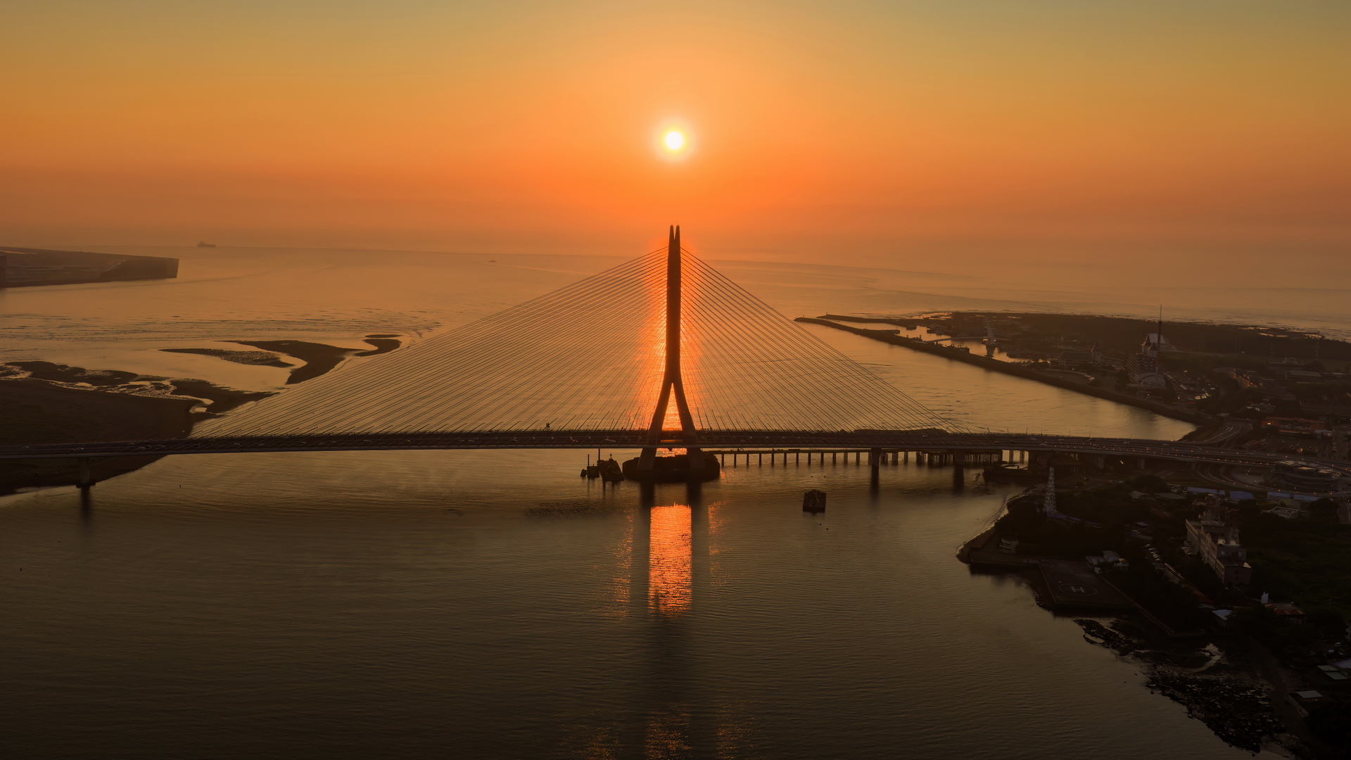 淡水河口的金黃夕照與宏偉的淡江大橋巧妙相遇，橋塔的俐落剪影與波光 粼粼的水面勾勒出專屬淡八地區的嶄新觀光地標。