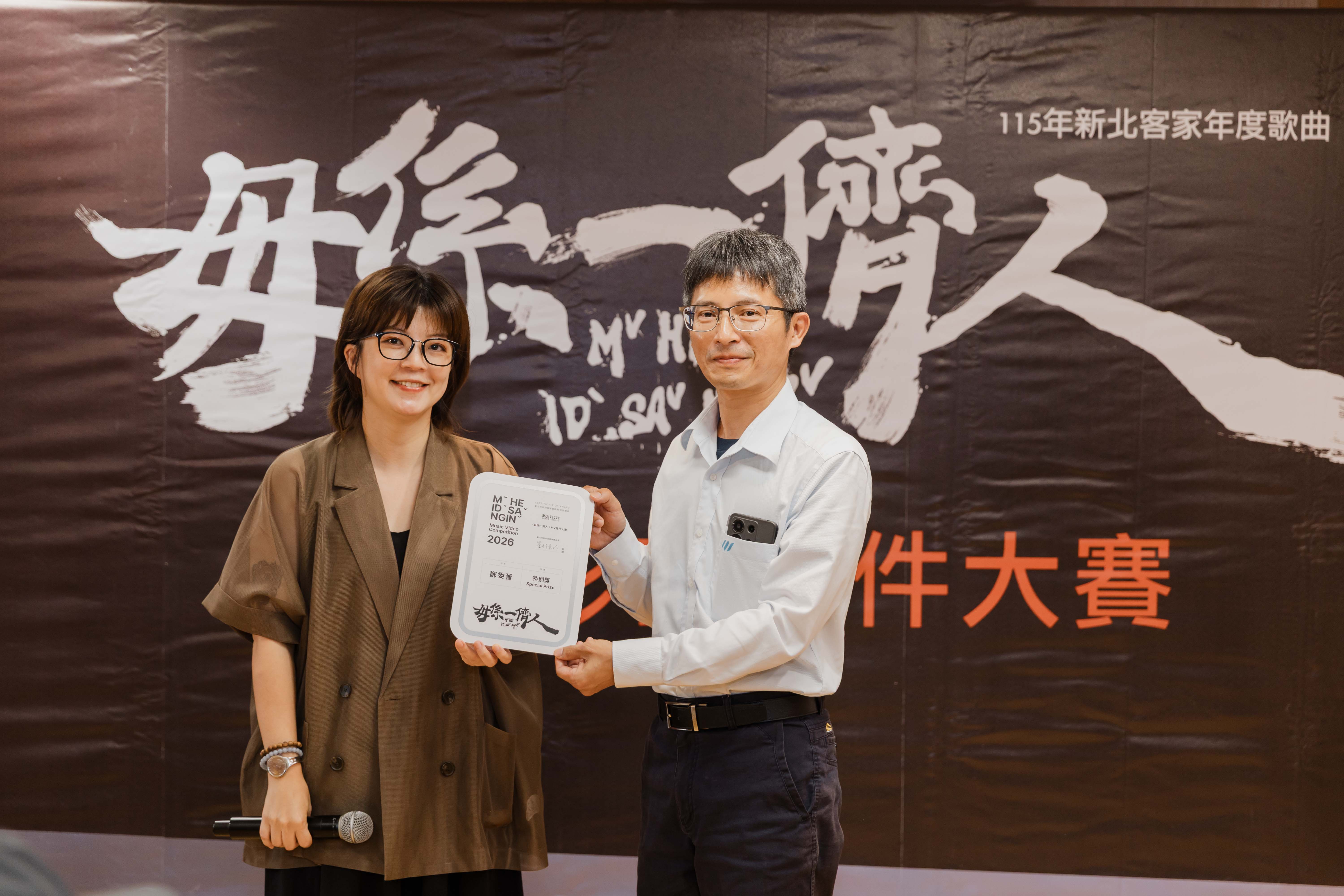圖5. 新北市客家事務局局長劉冠吟(左)與〈毋係一儕人〉MV短影音徵件比賽特別獎領獎代表(右)合影，紀念新北市捷運局工程管理科科長周茂益（芋仔Or）作品。