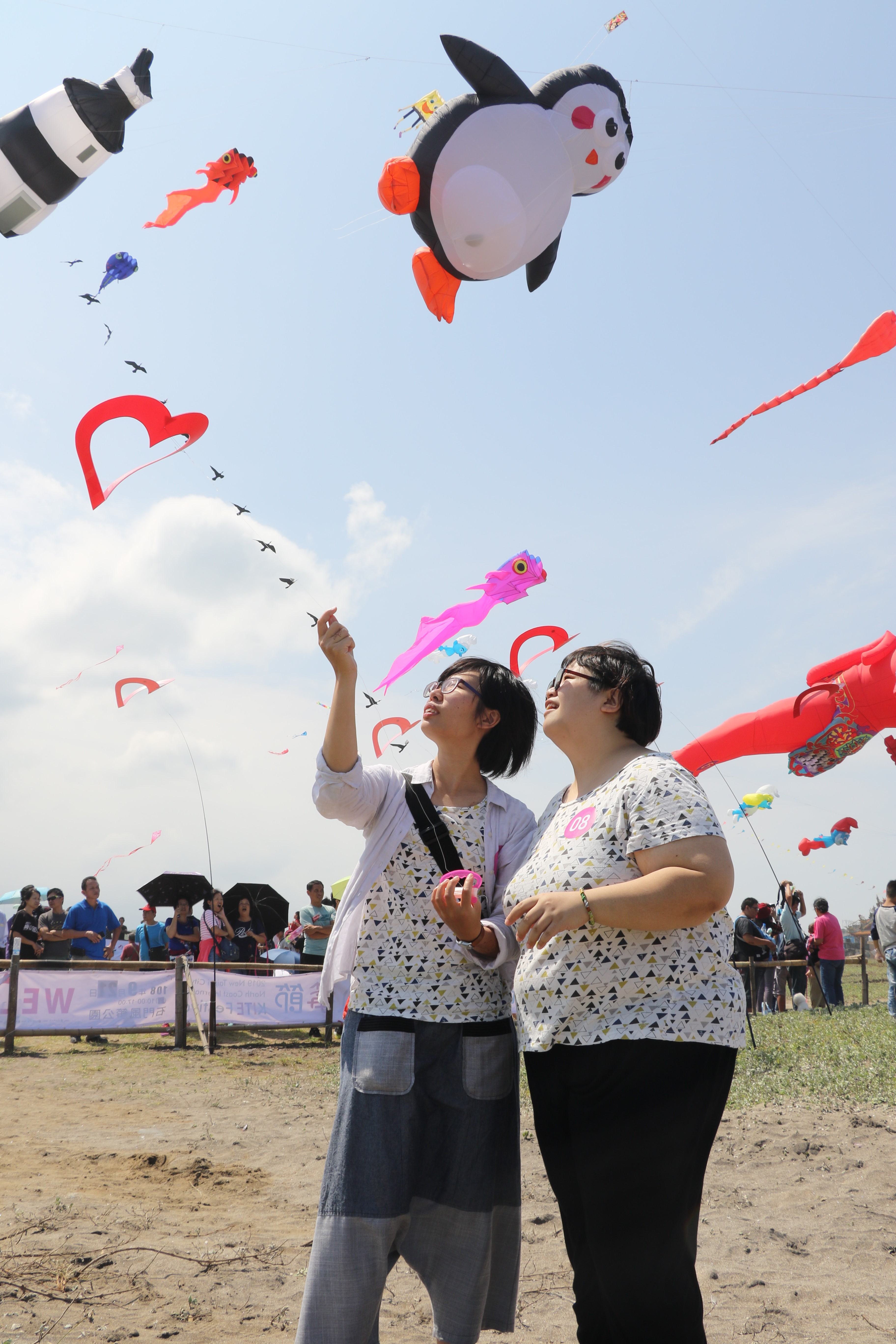 沐目（右）、小岑在國際風箏節一起施放心形風箏 背後是新北市性平CEO企鵝風箏