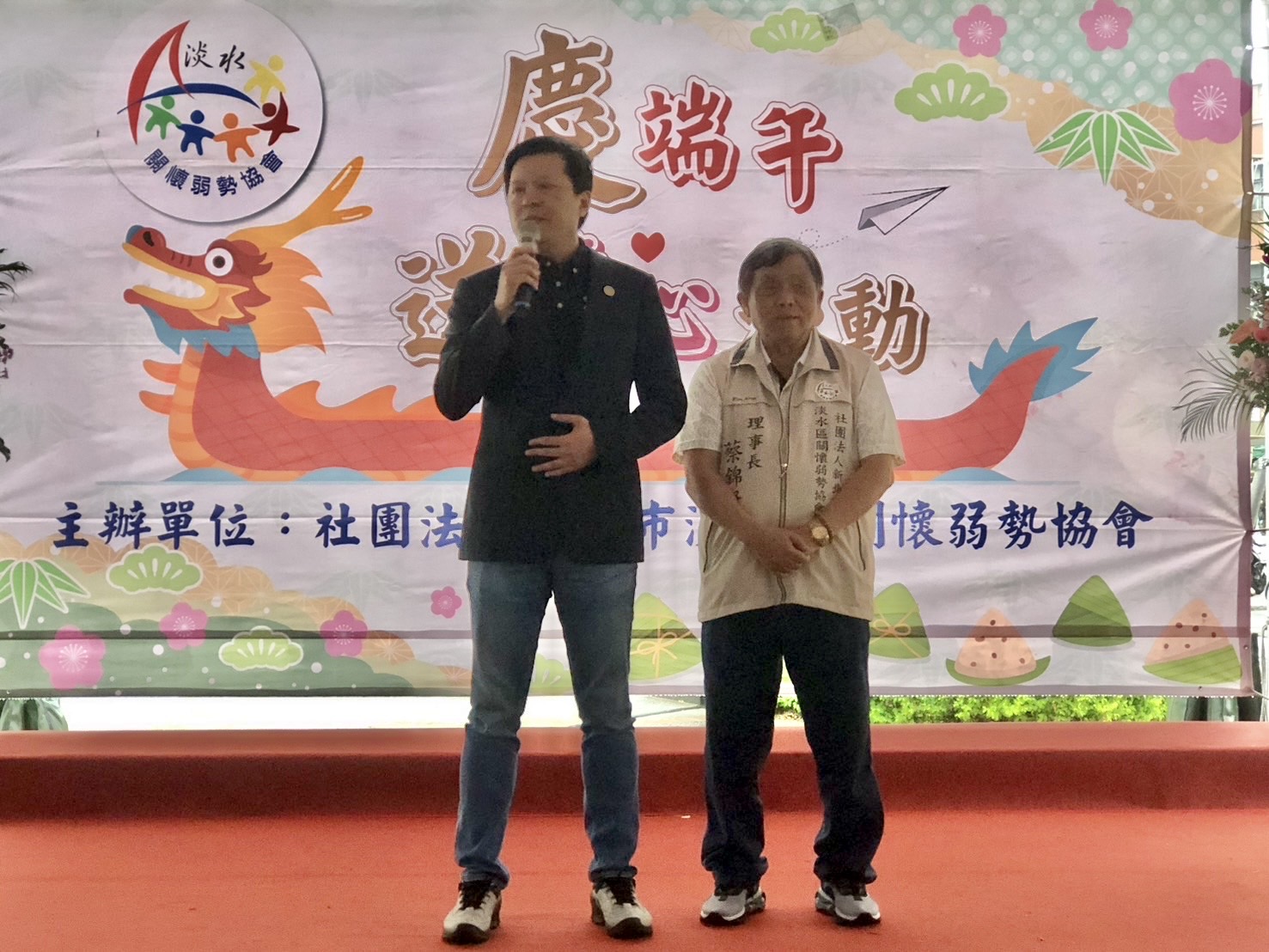 新北市副市長朱惕之(左)到場感謝淡水區關懷弱勢協會理事長蔡錦賢(右)及團隊,連續18年一年三節以實際行動幫助許多弱勢家庭及嘉惠北海岸清寒學子